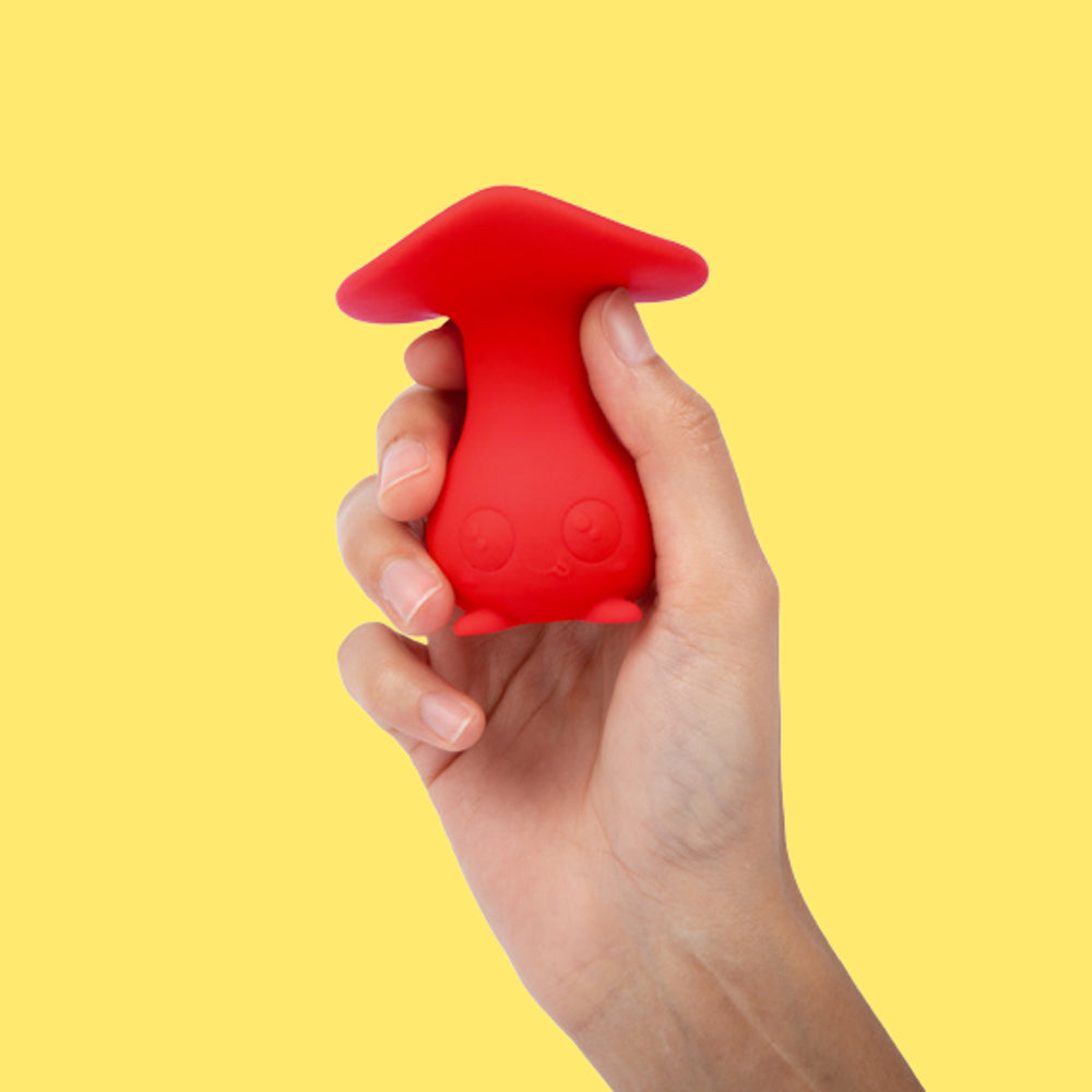 Red silicone mushroom-shaped product held in a hand against a yellow background