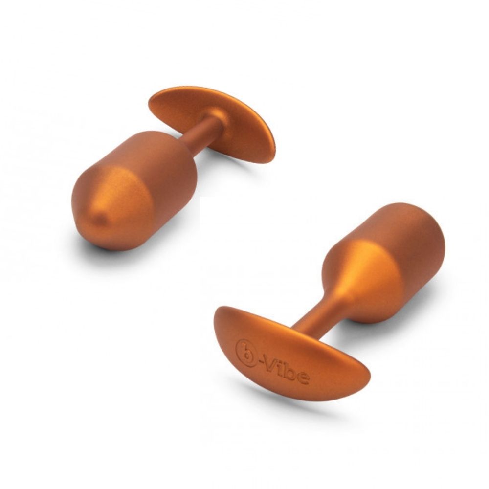 Two B-Vibe Snug Plugs 2 (M) - Limited Edition Sunburst Orange laying on their side, the one on the right has the tip in the forefront and the one on the left has the base in the forefront