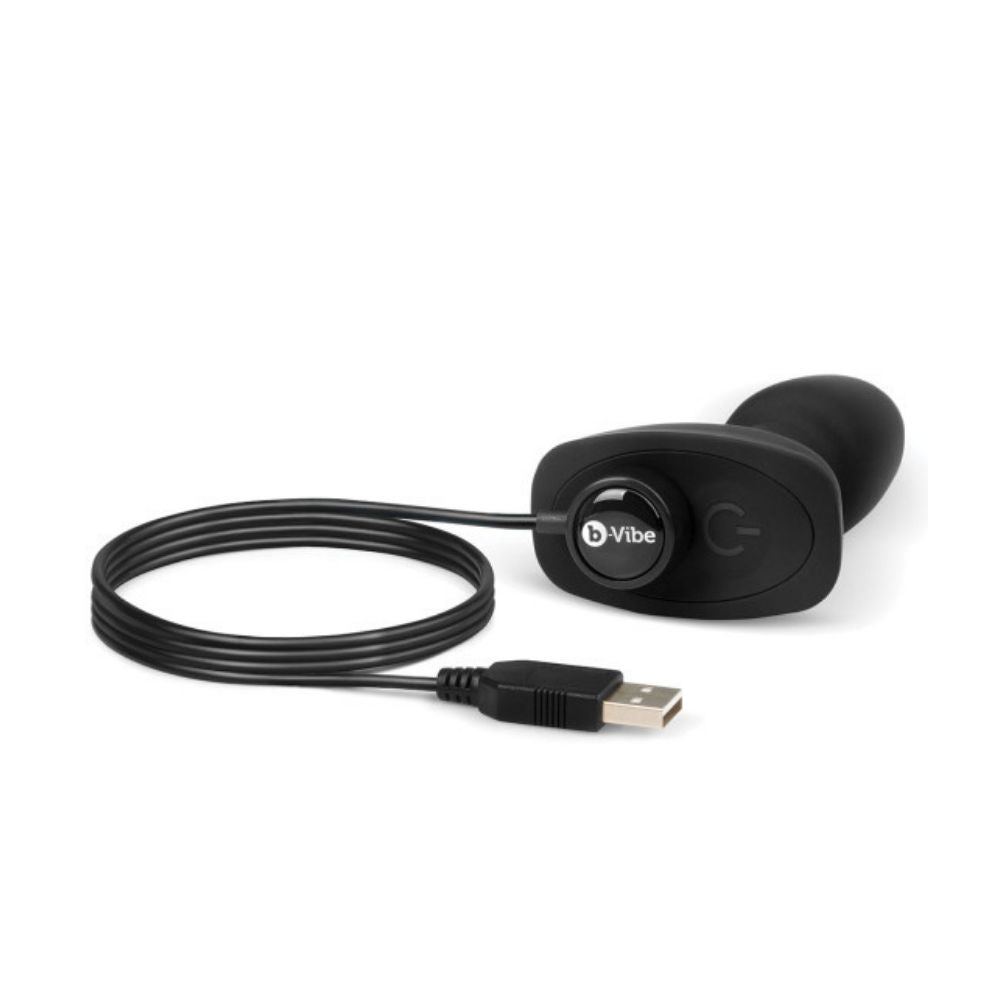 Black B-Vibe Rimming Petite Plug laying flat on its side with the charging cable plugged into the base