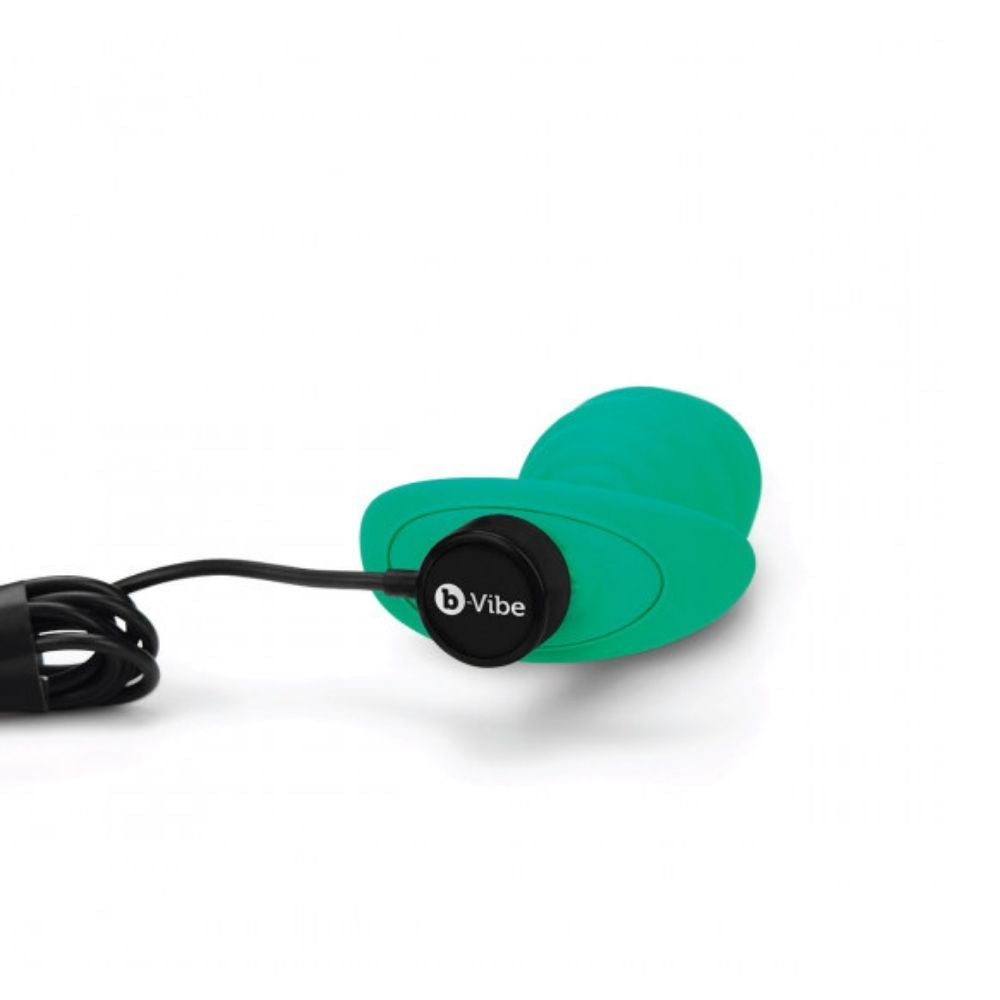 B-Vibe Texture Plug Twist Green (Large) laying flat with the charger plugged into its base