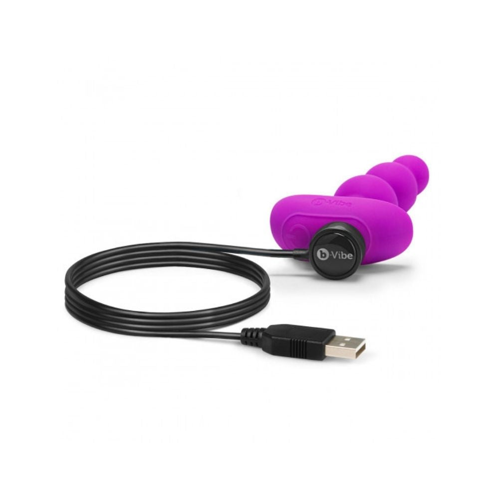 B-Vibe Triplet Beads laying flat on its side with the charger plugged into its base