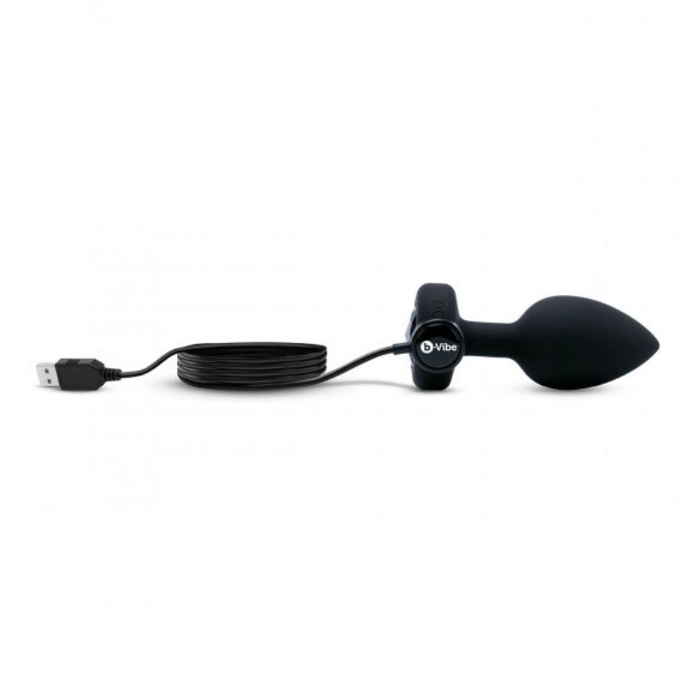 Black B-Vibe Vibrating Jewel Plug Medium/Large laying flat on its side with the charger plugged into its base