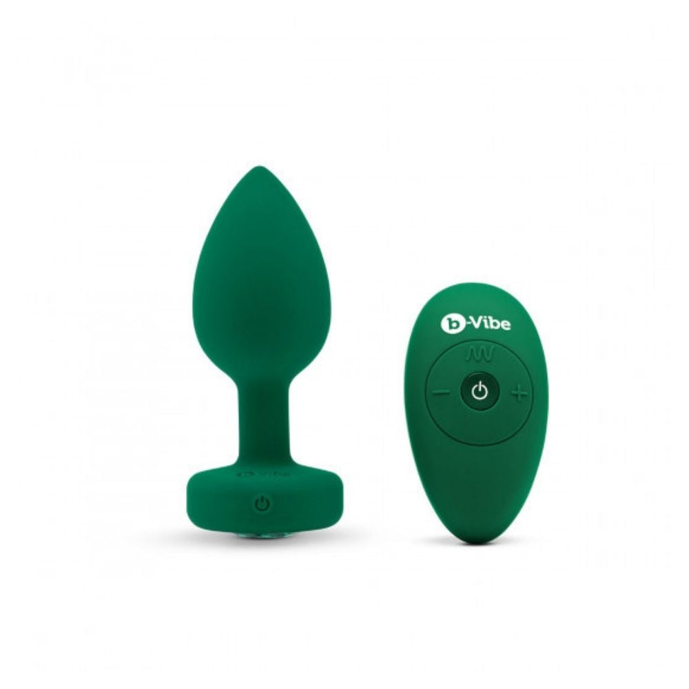 Emerald B-Vibe Vibrating Jewel Plug Medium/Large standing upright on its base beside the remote control it comes with