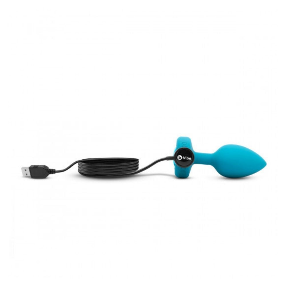 Aqua B-Vibe Vibrating Jewel Plug Small/Medium laying on its side with the charger plugged into its base