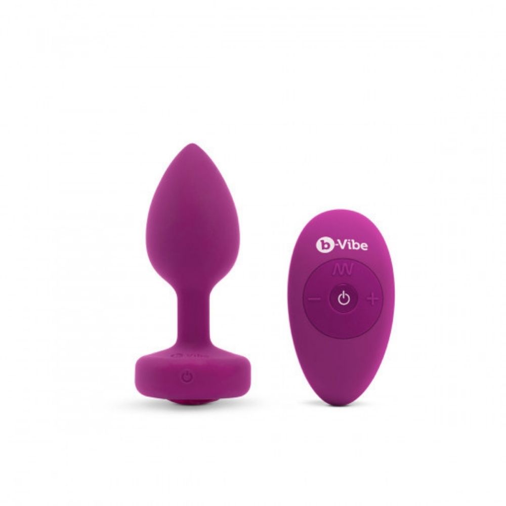Fuchsia B-Vibe Vibrating Jewel Plug Small/Medium standing upright on its base beside the remote control it comes with