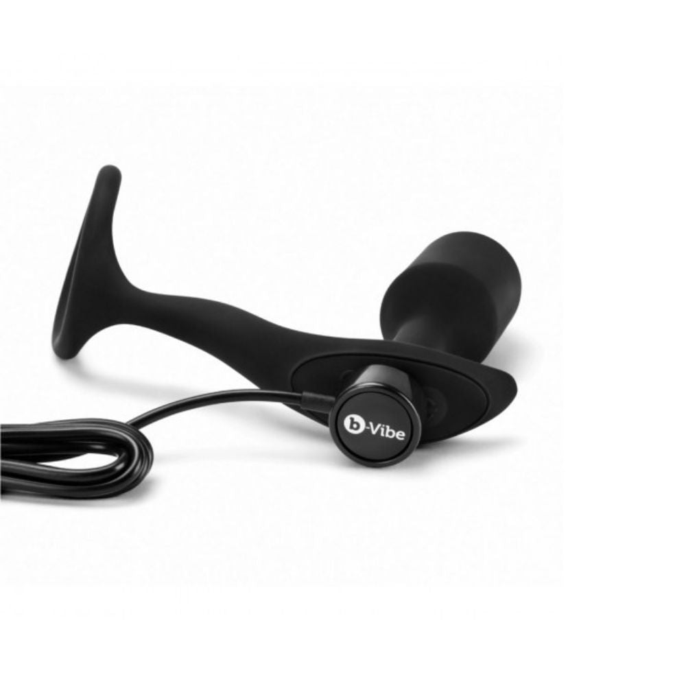 B-Vibe Vibrating Snug & Tug laying flat on its side with the charger plugged into its base