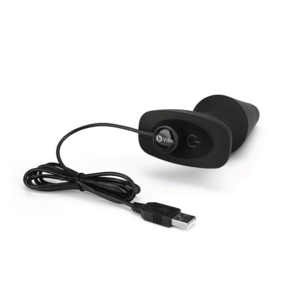 B-Vibe Rimming Plug XL laying flat on its side with the charger plugged into its base