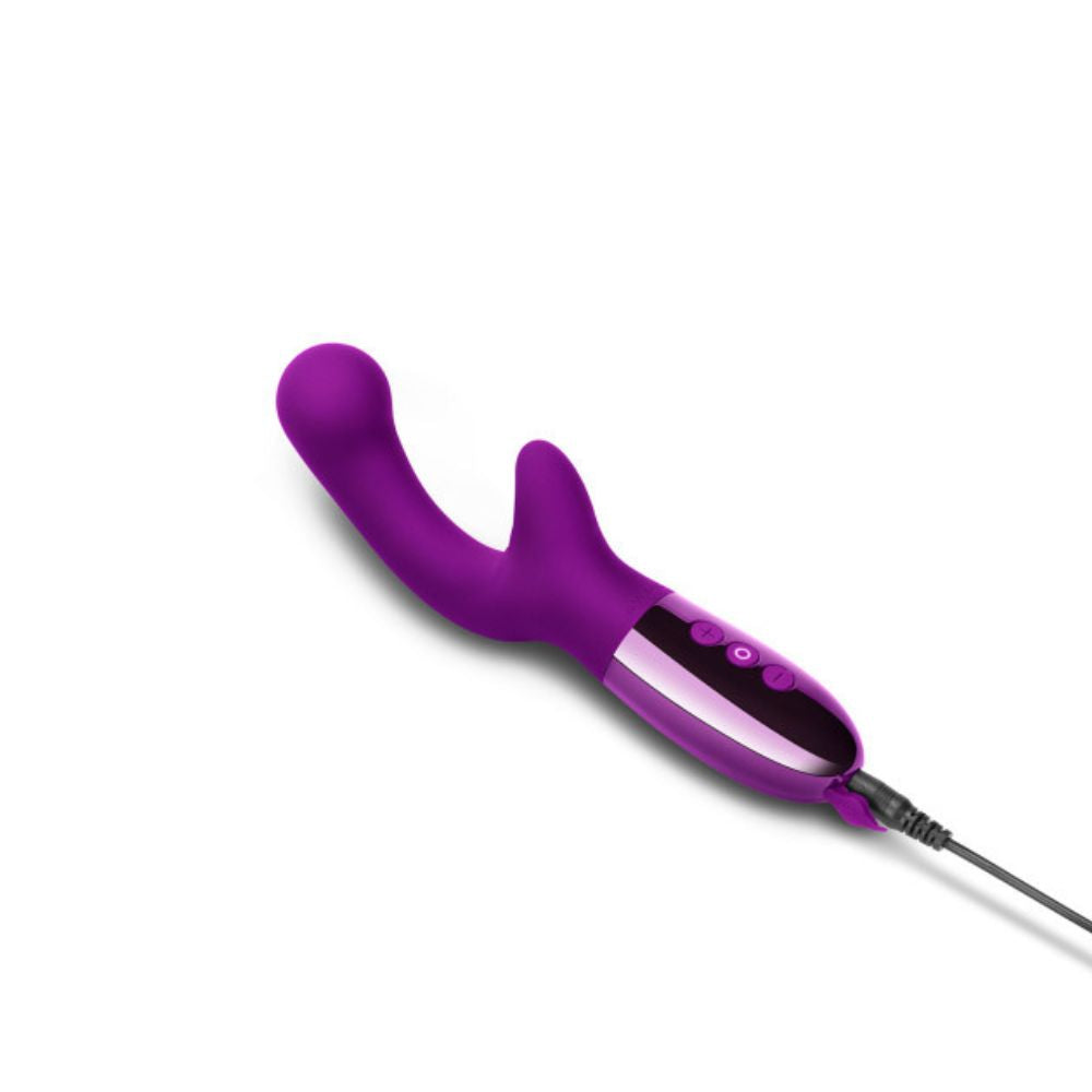 Le Wand Xo in dark cherry laying flat on its back side with the charger plugged into its base